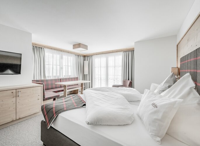 Suite mit Bergblick im Hotel Jenewein Helles Hotelzimmer mit Bett, Sitzbank und großen Fenstern im Hotel Jenewein.