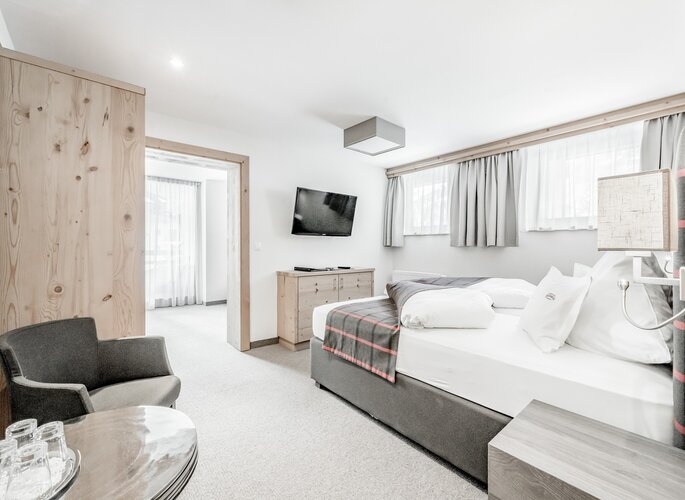Familienzimmer im Hotel Jenewein mit Sitzecke Helles Familienzimmer mit Doppelbett, Sitzecke, Fernseher und Holzmöbeln.