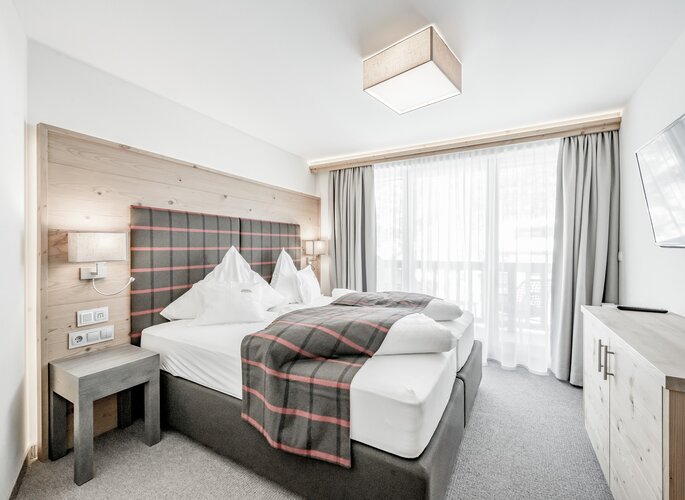 Familienzimmer West im Hotel Jenewein Helles Familienzimmer mit Doppelbett, Holzdetails und großem Fenster im Hotel Jenewein.