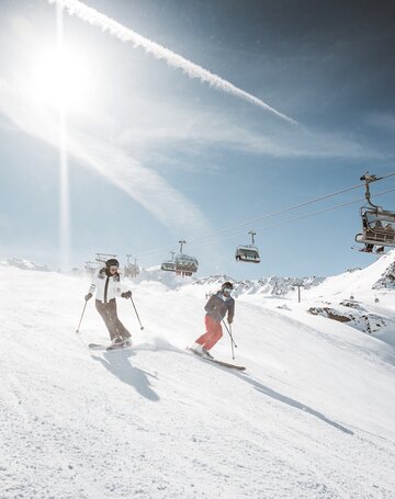 Skiurlaub an der Piste in Obergurgl Zwei Skifahrer fahren auf einer sonnigen Skipiste unter einem Sessellift ab.
